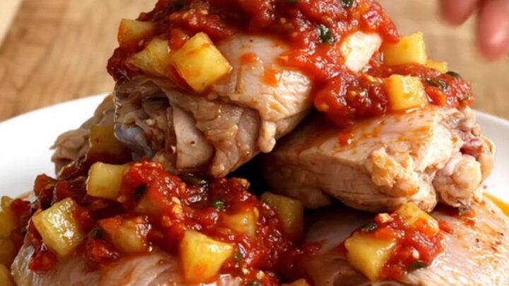 A white oval plate featuring tender chicken thighs topped with chunky pineapple and red salsa.