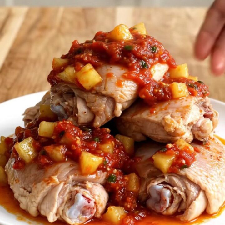 A white oval plate featuring tender chicken thighs topped with chunky pineapple and red salsa.
