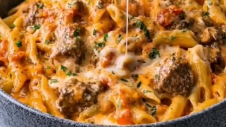 A close-up of a fork lifting creamy penne pasta with a dramatic mozzarella cheese pull in a dark bowl.