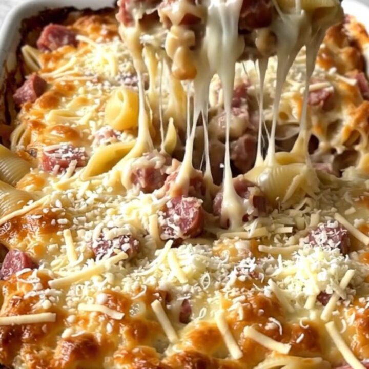 A golden, bubbling pasta bake in a white ceramic dish filled with shells, sausage, and broccoli.
