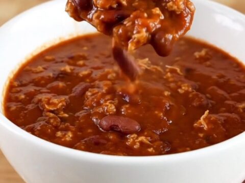 A white bowl filled with dark, rich Cincinnati-style turkey chili served on a light wooden table.