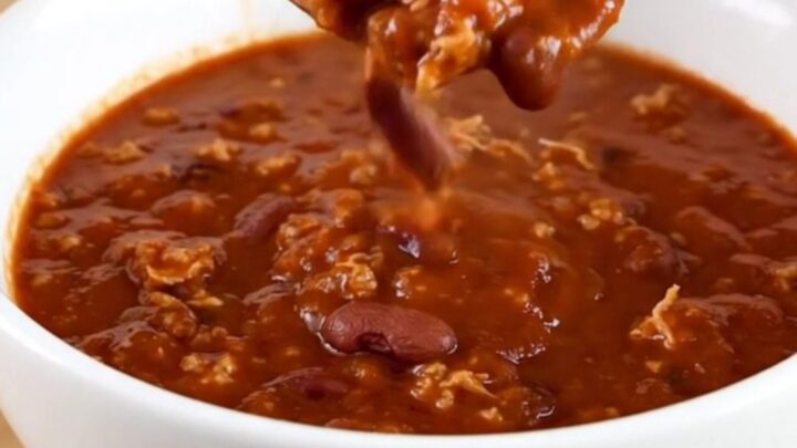 A white bowl filled with dark, rich Cincinnati-style turkey chili served on a light wooden table.