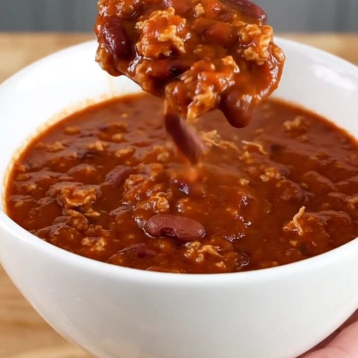 A white bowl filled with dark, rich Cincinnati-style turkey chili served on a light wooden table.