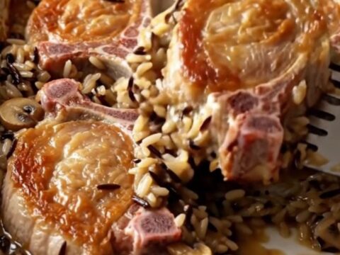 A golden-brown baked pork chop served over a bed of creamy wild rice in a white ceramic dish.