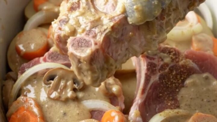 A close-up of a slow cooker filled with tender bone-in pork chops, sliced potatoes, and carrots in a creamy mushroom sauce.
