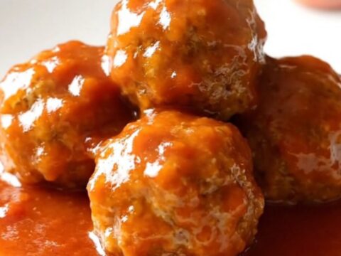 A close-up of tender ham balls covered in a glossy, sweet tomato and brown sugar sauce in a slow cooker.