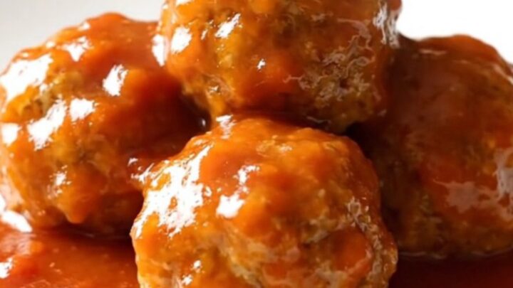 A close-up of tender ham balls covered in a glossy, sweet tomato and brown sugar sauce in a slow cooker.