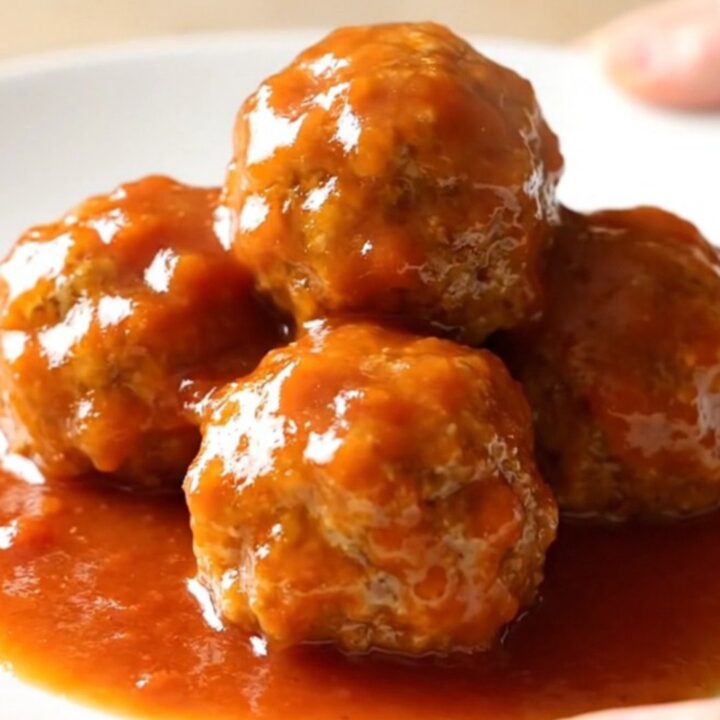 A close-up of tender ham balls covered in a glossy, sweet tomato and brown sugar sauce in a slow cooker.