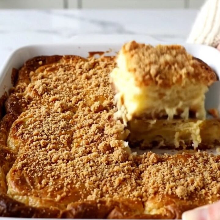 A golden brown, puffed eggnog French toast bake in a white ceramic dish on a speckled countertop.