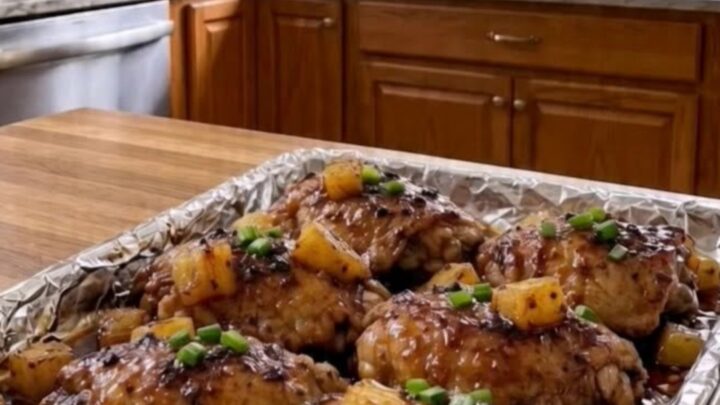 Sticky Hawaiian chicken thighs with caramelized skin, garnished with pineapple and scallions on a sheet pan.