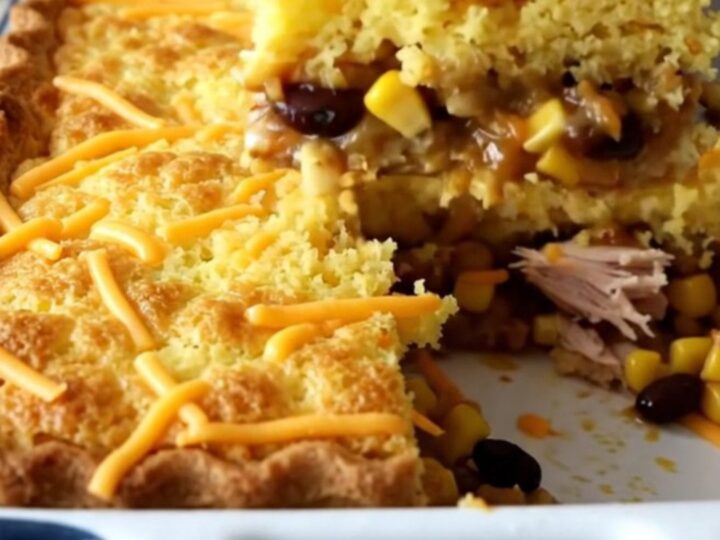 A golden-brown baked tamale pie in a white rectangular dish, showing a cornbread crust and savory turkey filling.