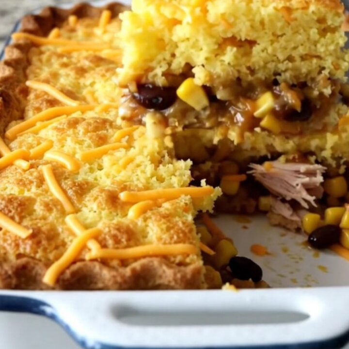 A golden-brown baked tamale pie in a white rectangular dish, showing a cornbread crust and savory turkey filling.