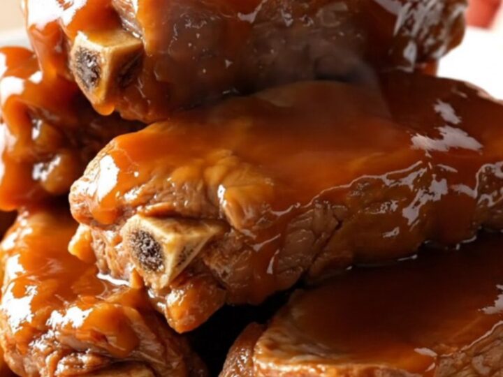 A close-up of tender, glazed country-style pork ribs with pineapple chunks on a white plate.