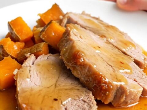A slow cooker filled with hot honey glazed pork tenderloin and chunks of sweet potatoes on a white counter.
