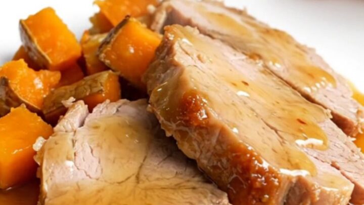 A slow cooker filled with hot honey glazed pork tenderloin and chunks of sweet potatoes on a white counter.
