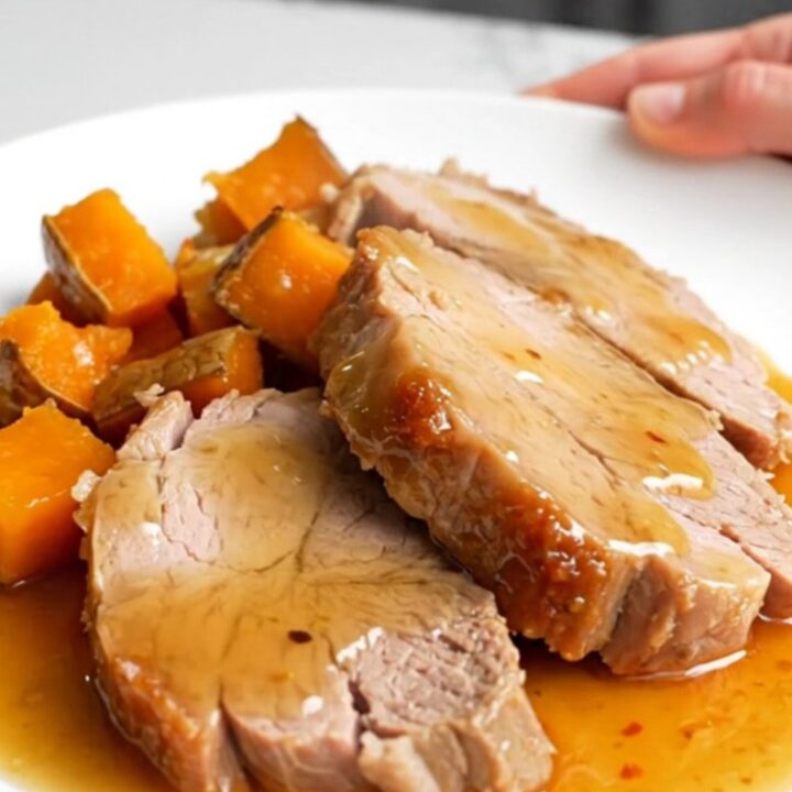 A slow cooker filled with hot honey glazed pork tenderloin and chunks of sweet potatoes on a white counter.