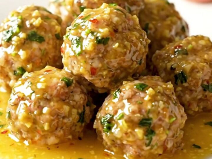 A close-up of tender turkey meatballs coated in a glossy golden garlic butter sauce with fresh parsley.