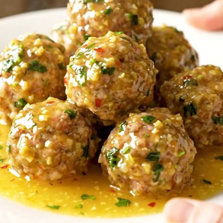 A close-up of tender turkey meatballs coated in a glossy golden garlic butter sauce with fresh parsley.