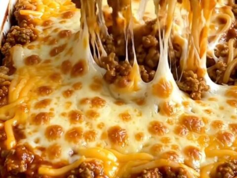 A rectangular ceramic baking dish filled with a baked Cincinnati chili spaghetti bake topped with melted cheddar.