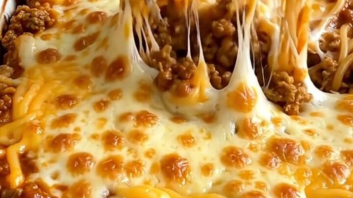 A rectangular ceramic baking dish filled with a baked Cincinnati chili spaghetti bake topped with melted cheddar.
