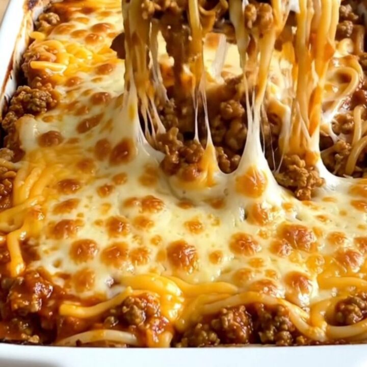 A rectangular ceramic baking dish filled with a baked Cincinnati chili spaghetti bake topped with melted cheddar.