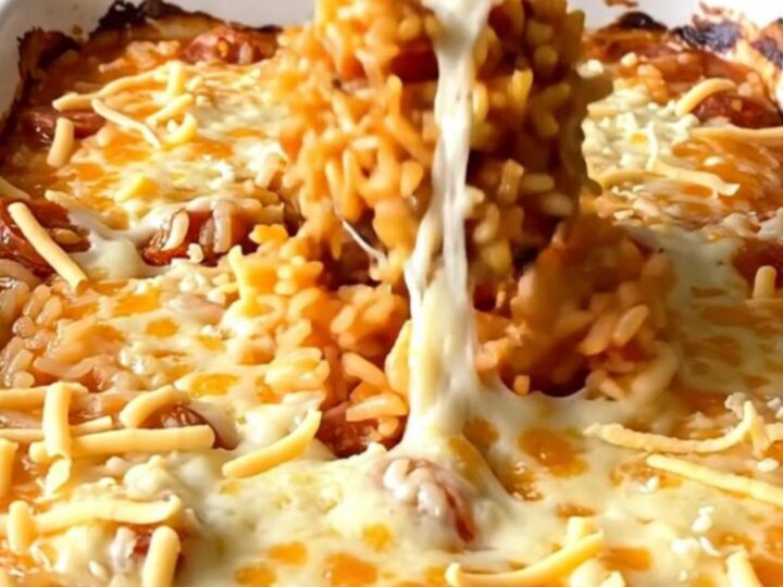 A top-down view of a rectangular baking dish filled with raw rice, crumbled chorizo, tomato broth, and shredded cheese.