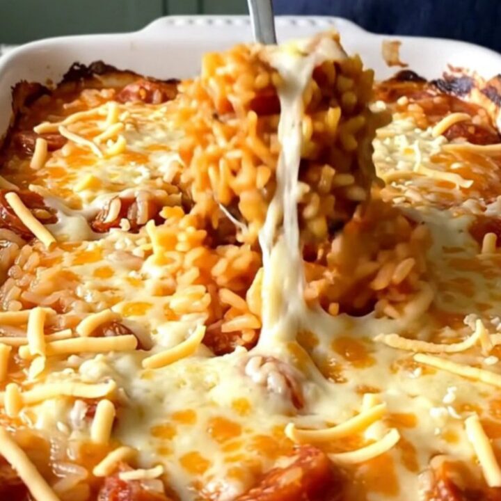 A top-down view of a rectangular baking dish filled with raw rice, crumbled chorizo, tomato broth, and shredded cheese.