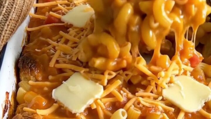 A large white enameled baker filled with golden, bubbling tomato mac and cheese on a granite countertop.