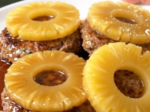 Six ground turkey patties topped with pineapple rings in a black slow cooker insert.