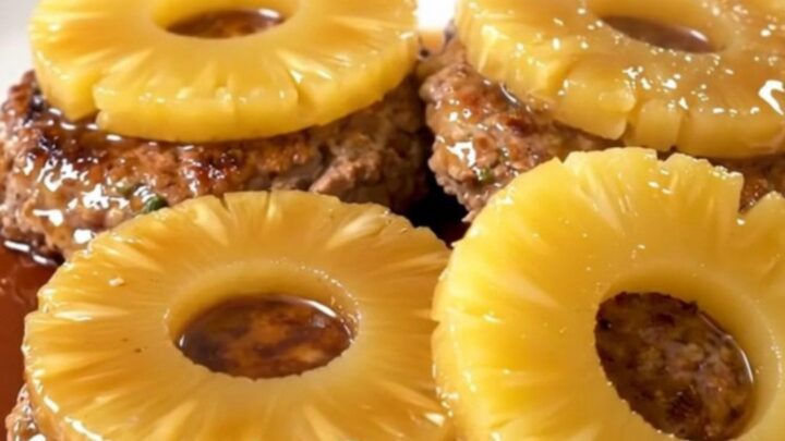 Six ground turkey patties topped with pineapple rings in a black slow cooker insert.