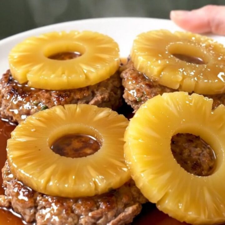 Six ground turkey patties topped with pineapple rings in a black slow cooker insert.