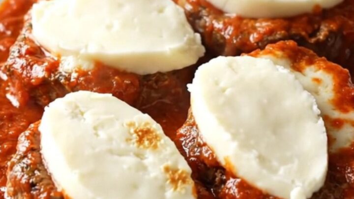 A close-up of a tender beef cube steak topped with thick marinara sauce and melted mozzarella cheese in a slow cooker.