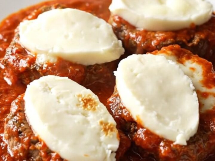 A close-up of a tender beef cube steak topped with thick marinara sauce and melted mozzarella cheese in a slow cooker.