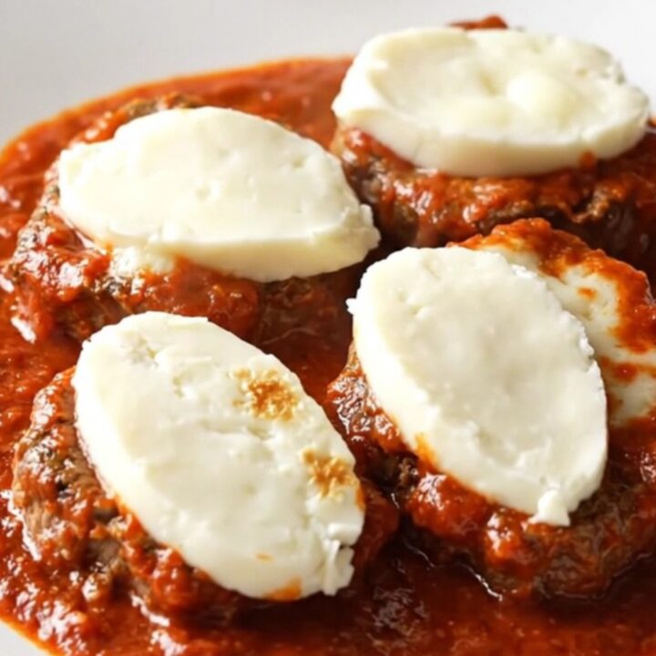 A close-up of a tender beef cube steak topped with thick marinara sauce and melted mozzarella cheese in a slow cooker.