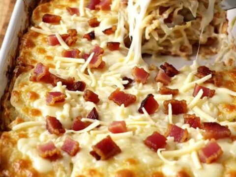 A golden, bubbling dish of scalloped potatoes with visible bacon bits and melted mozzarella cheese.