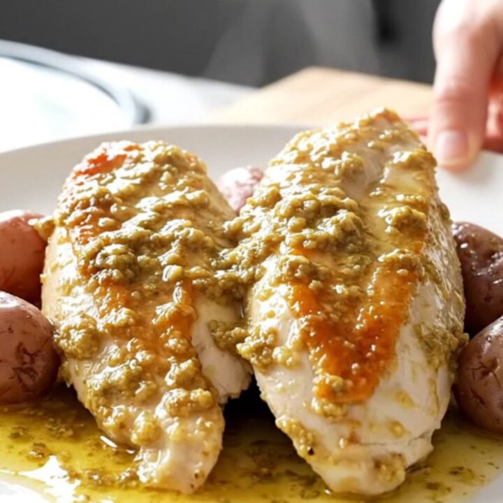 A white oval slow cooker filled with tender chicken breasts and baby red potatoes in a light herb butter sauce.