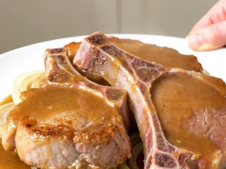 A close-up of tender bone-in pork chops covered in a rich, savory beer and onion gravy on a white plate.