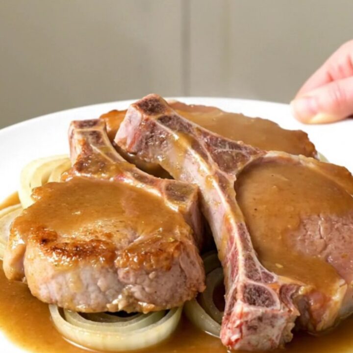 A close-up of tender bone-in pork chops covered in a rich, savory beer and onion gravy on a white plate.