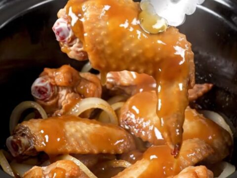 A close-up of honey BBQ turkey wings in a slow cooker, looking tender and coated in a thick, glossy sauce.
