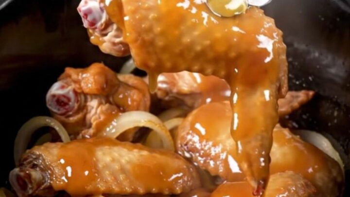 A close-up of honey BBQ turkey wings in a slow cooker, looking tender and coated in a thick, glossy sauce.