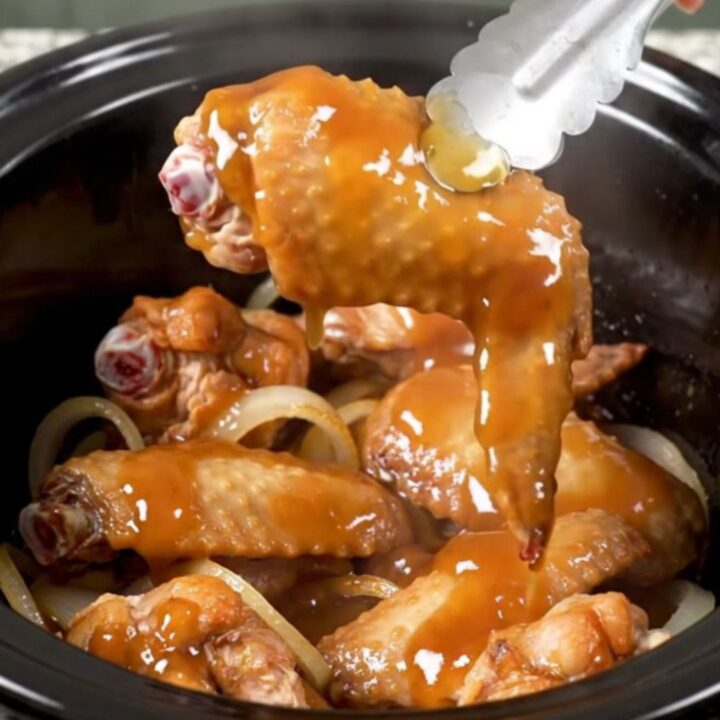 A close-up of honey BBQ turkey wings in a slow cooker, looking tender and coated in a thick, glossy sauce.