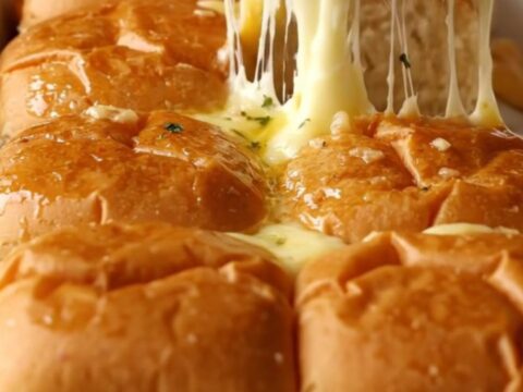 A rectangular baking dish filled with golden brown, buttery garlic grilled cheese sliders.