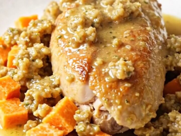 A close-up of a tender chicken breast served with roasted sweet potato cubes and savory herb stuffing on a white plate.