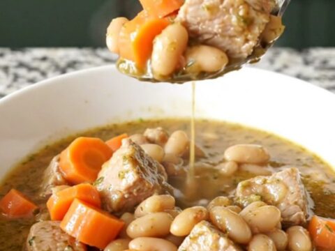 A bowl of hearty pork and white bean stew with visible carrot slices and herbs.