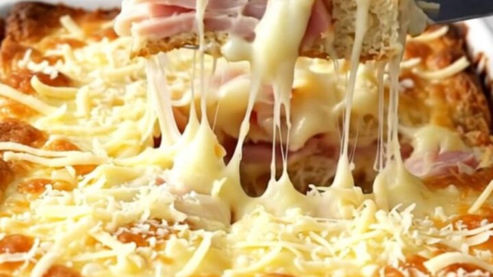 A golden, bubbling Monte Cristo breakfast casserole in a white ceramic dish.
