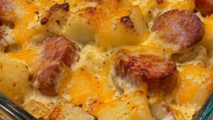 A glass baking dish filled with bubbling creamy potatoes, browned sausage slices, and golden melted cheddar cheese.