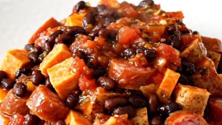 A top-down view of a slow cooker filled with smoked sausage, sweet potato cubes, and black beans in a vibrant salsa sauce.
