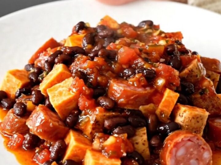 A top-down view of a slow cooker filled with smoked sausage, sweet potato cubes, and black beans in a vibrant salsa sauce.