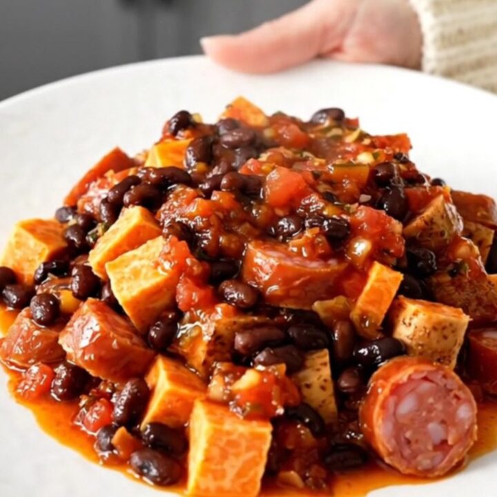 A top-down view of a slow cooker filled with smoked sausage, sweet potato cubes, and black beans in a vibrant salsa sauce.