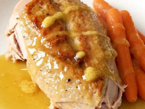 A whole boneless turkey breast and baby carrots in a slow cooker with a honey butter glaze.